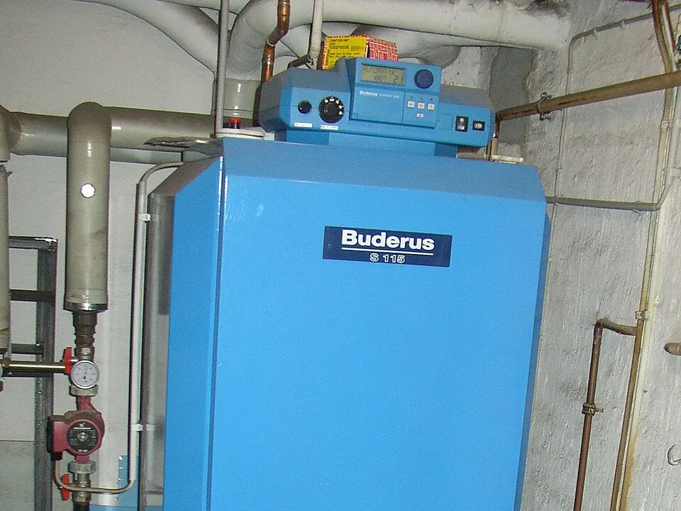 Une chaudière murale bleue installée dans une cave, raccordée à ses conduites.
