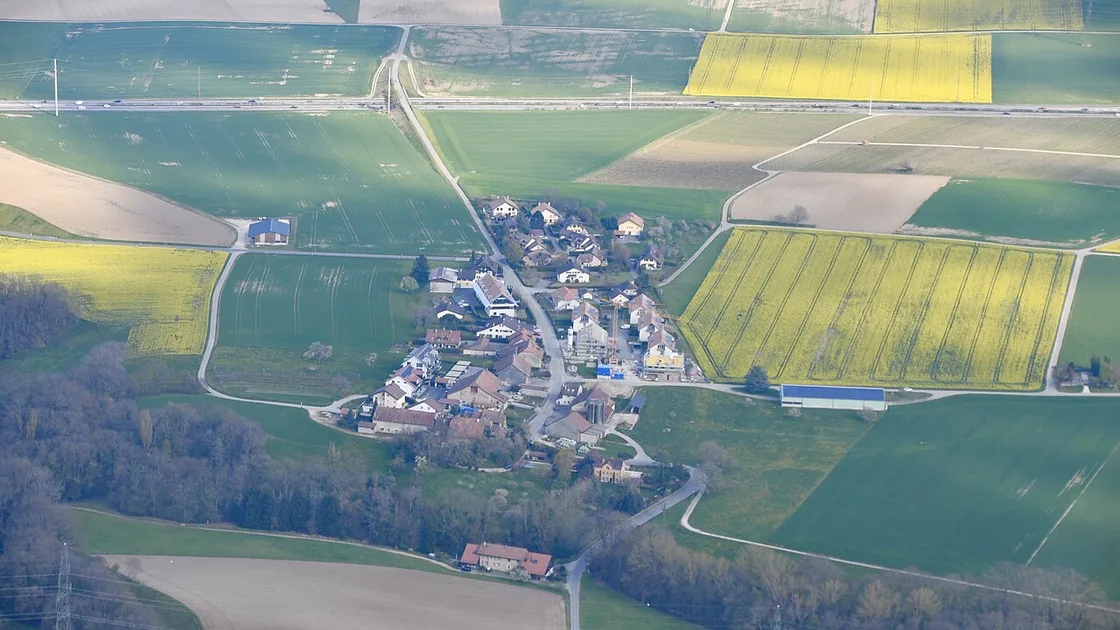 Vue aérienne du village d'Arnex-sur-Nyon posé au milieu de champs cultivés