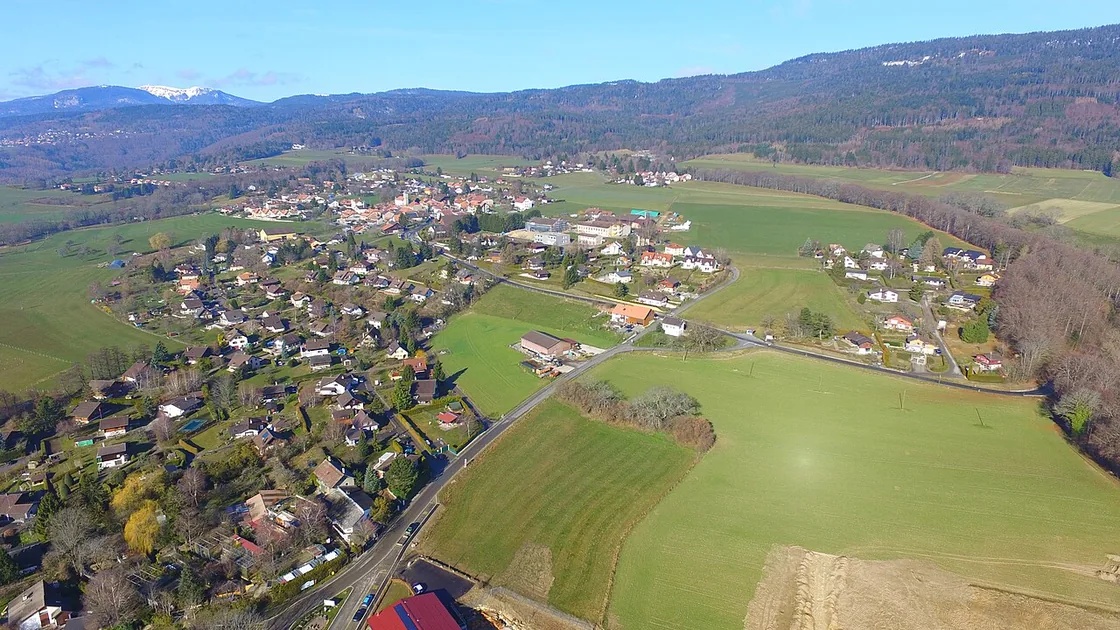 Vue aérienne du village du Vaud, champs et forêts du Jura derrière