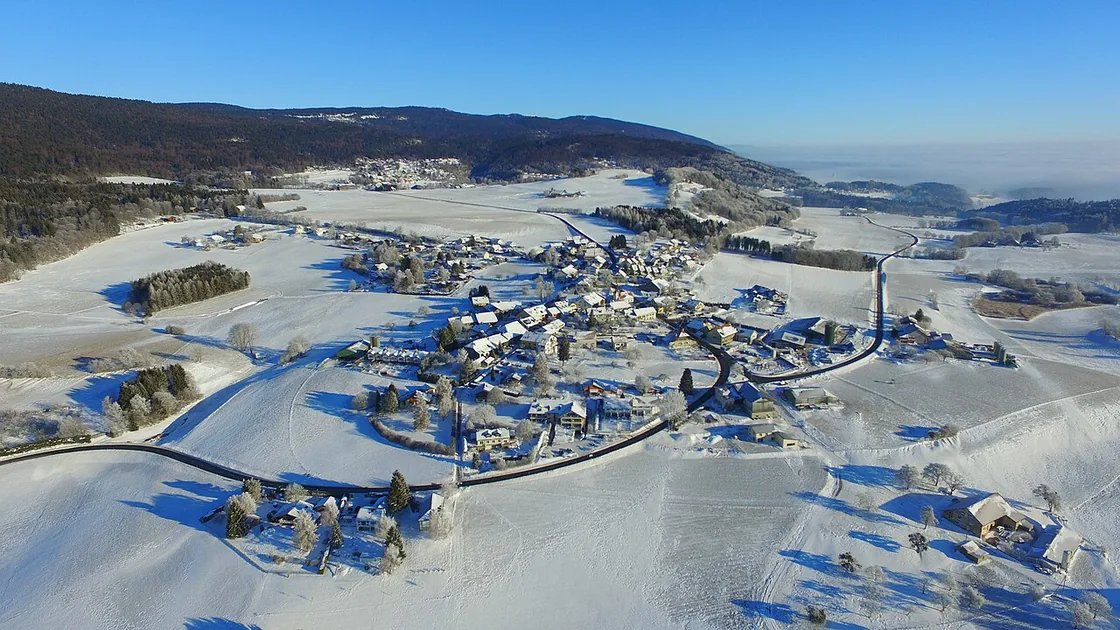 Vue aérienne de Longirod sous la neige, ses toits blancs au milieu des champs