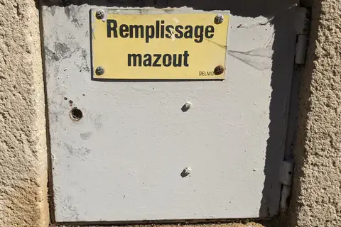 Une plaque de remplissage de mazout scellée sur un mur, rouillée.