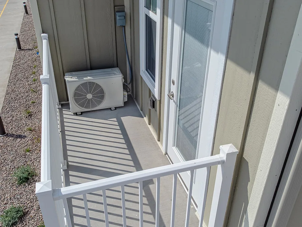 Une unité extérieure de pompe à chaleur installée sur un balcon, contre un garde-corps.
